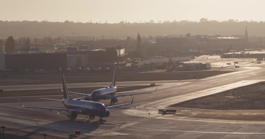 Two passenger jets wait on the airport tarmac as the sun sets in the hazy distance