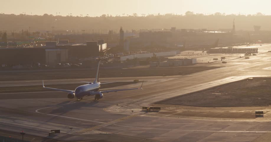 A passenger airplane taxis on the runway at a large airport during a hazy sunset