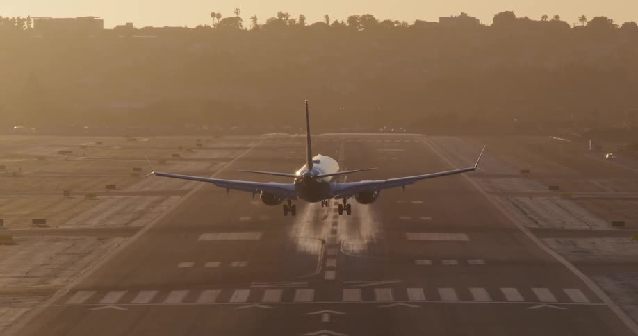 A slow-motion, symmetrical shot captures a commercial jetliner landing on a hazy runway during a golden sunrise