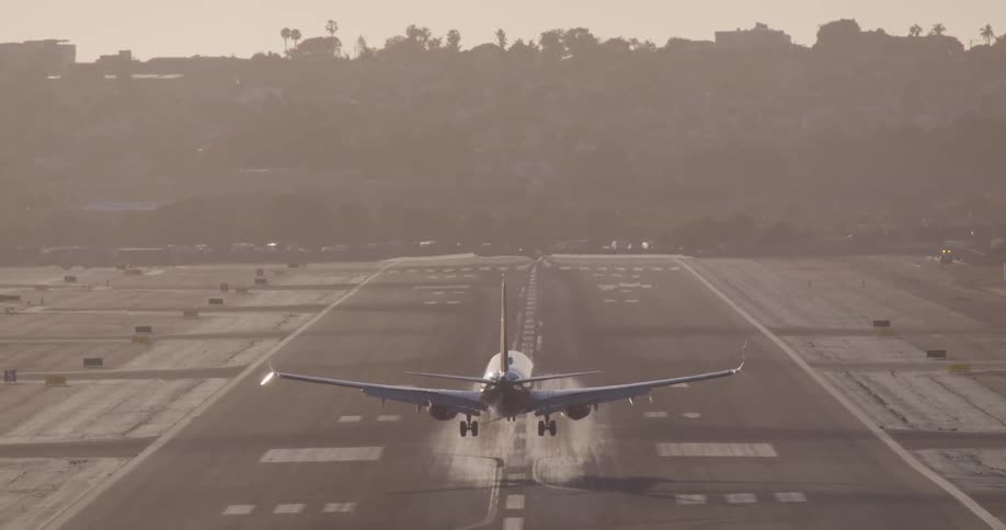 A commercial airplane descends and lands on a runway in dramatic slow motion as smoke puffs from the tires upon touchdown