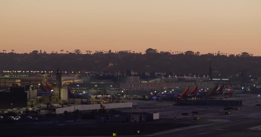 A static, wide view of a busy airport terminal with airplanes at their gates as the sky glows during dusk
