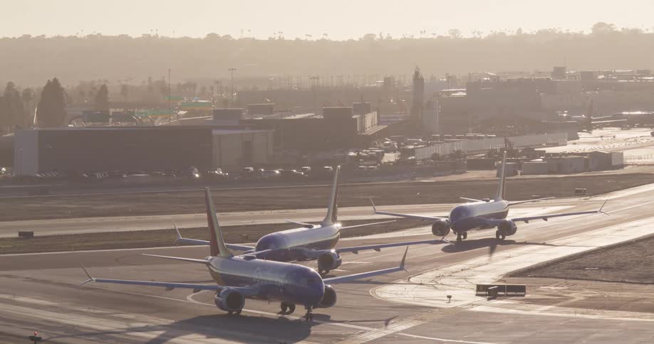 A trio of commercial airplanes waits in line on a hazy airport runway during the golden hour