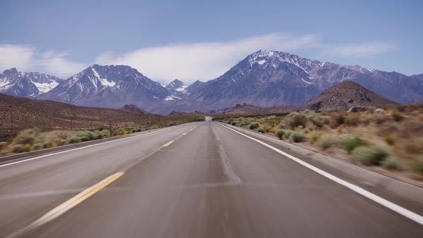A high-speed point-of-view shot driving down a long, empty desert road towards majestic snow-capped mountains
