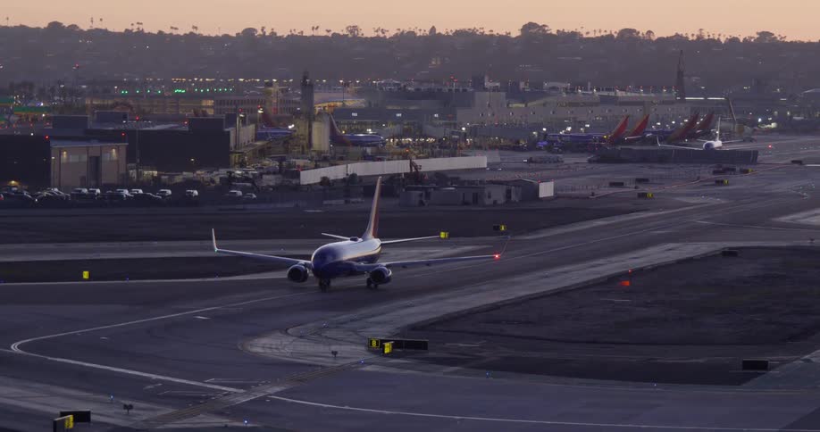 A passenger airplane taxis on the runway at a busy airport with city lights in the background during twilight
