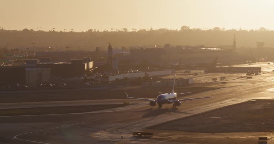 A commercial airliner slowly taxis on the runway during a hazy golden hour sunset