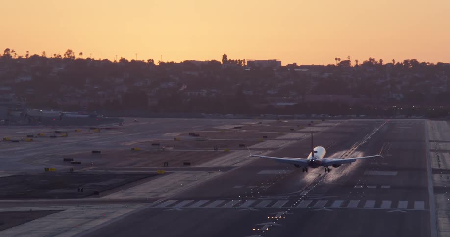 A passenger airplane glides in for a slow-motion landing on an airport runway as the sun sets