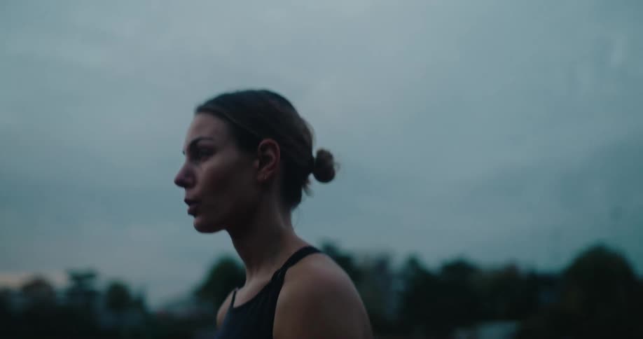 A determined female athlete takes a moment to herself on an empty running track at dusk before starting her training