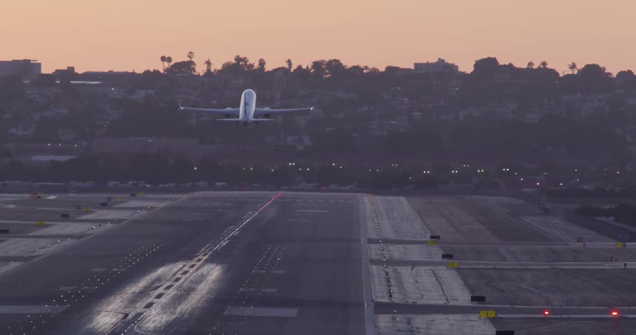 A passenger jet accelerates down a long runway and lifts off into the air during a hazy sunset