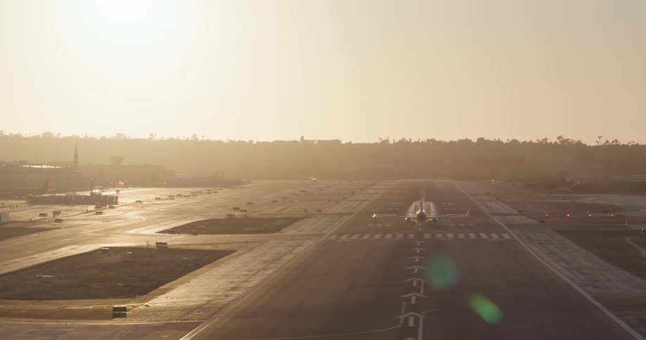 A commercial airliner takes off from the runway into the bright, hazy morning sun