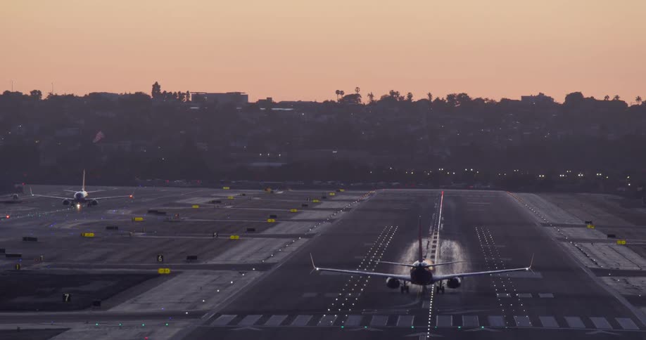 A commercial airliner taxis onto a runway and takes off into the beautiful twilight sky over a city