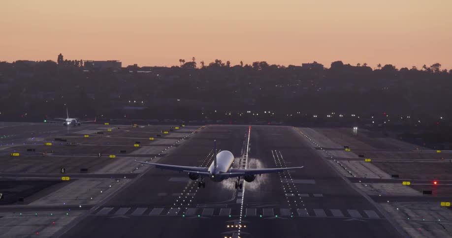 A passenger jet seen from behind makes a smooth landing on an illuminated runway at dusk