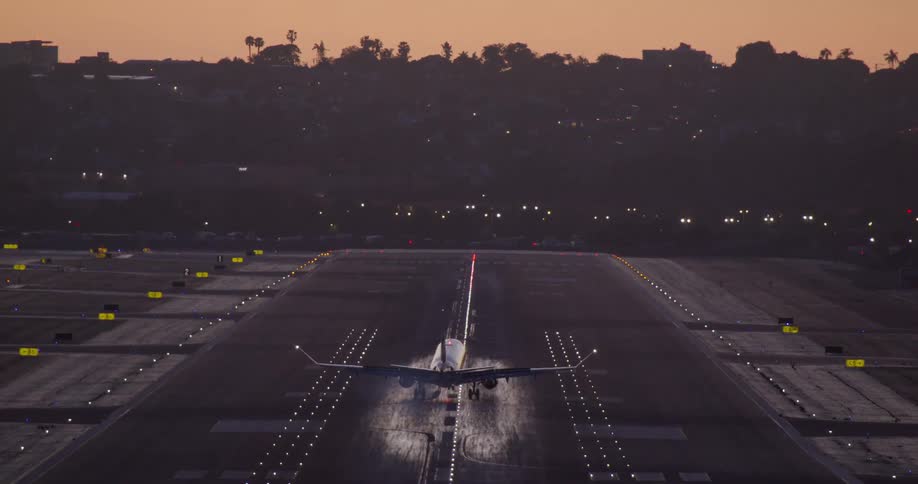 A passenger airplane makes a dramatic slow-motion landing on an illuminated runway at sunset