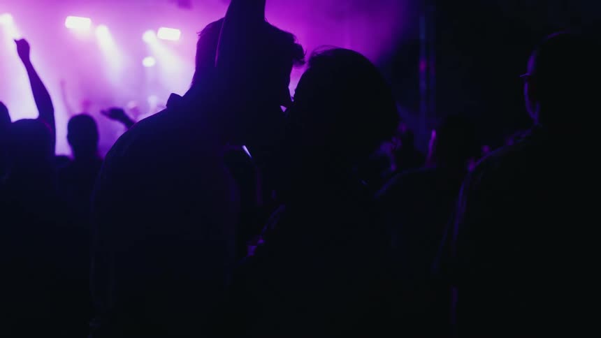 A silhouetted couple dances and embraces in slow motion in the crowd at a vibrant nighttime music festival