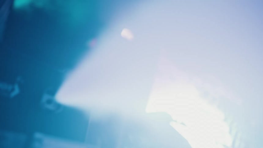 A fog machine releases a thick cloud of smoke illuminated by dramatic blue and teal stage lights during a live event