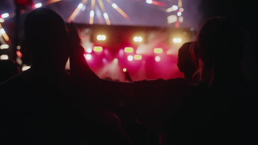 Slow motion shot of a silhouetted couple embracing while watching an energetic concert with colorful stage lights