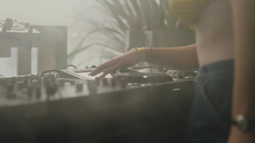 Atmospheric close-up of a female DJ's hands on the mixing console while she plays a set at a foggy party