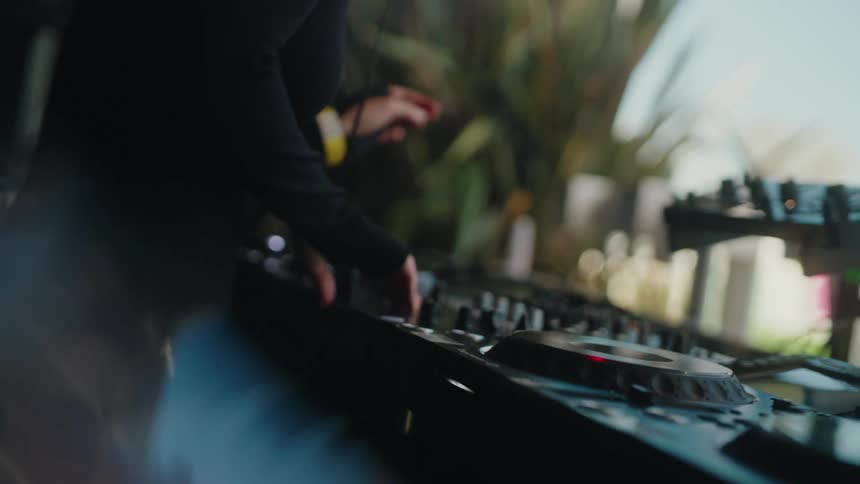 Close-up slow motion shot of a female DJ's hands working the knobs and faders on a mixer at a vibrant party
