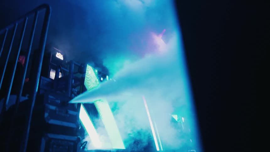 Atmospheric blue smoke billows from a machine backstage at an energetic night event
