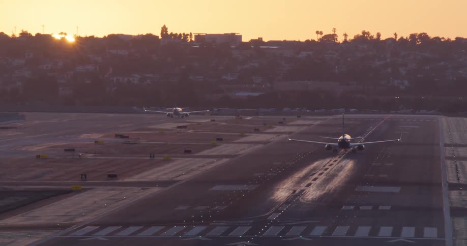 A passenger jet accelerates down a runway and takes off into the sky as the sun sets on the horizon