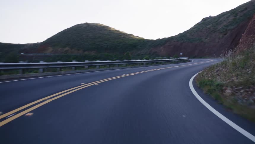 POV driving on a scenic winding road through the green coastal hills at dusk