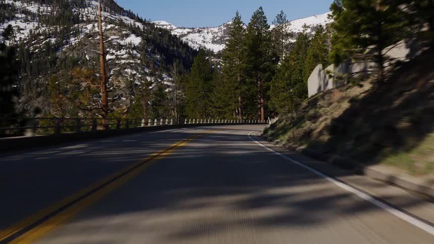 A scenic point-of-view drive along a winding mountain highway with snow-capped peaks in the distance