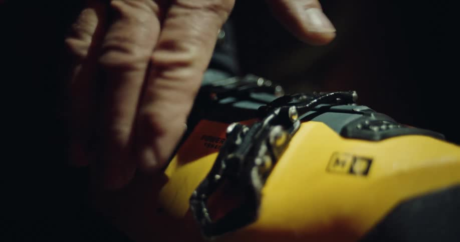 A close-up shot of a hand fastening the buckles on a yellow and black ski boot in slow motion
