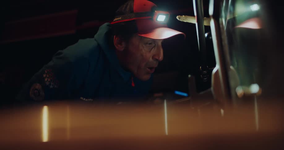 Close up of a man in a headlamp carefully servicing a ski in a dark workshop