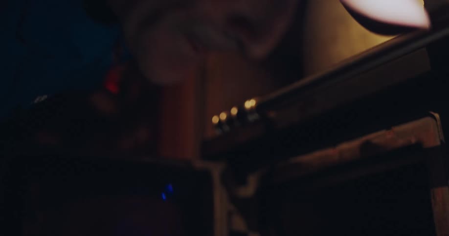 A focused mountain guide wearing a headlamp works diligently on equipment in his dark workshop