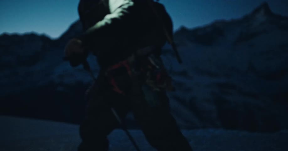 A lone mountain climber with a headlamp ascends a snowy peak in the pre-dawn darkness