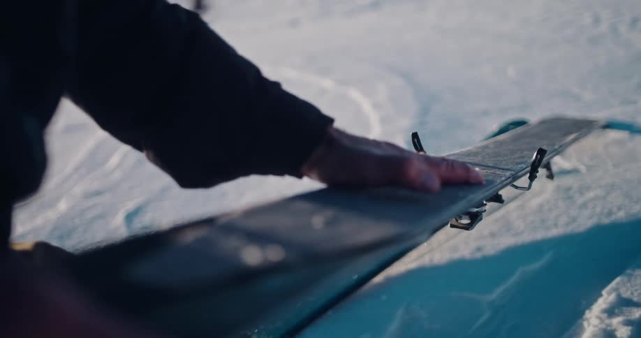 Close-up slow motion of a backcountry skier carefully applying a climbing skin to their ski in the snow