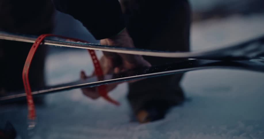 A skier carefully applies a climbing skin to the bottom of their ski in the snow in slow motion