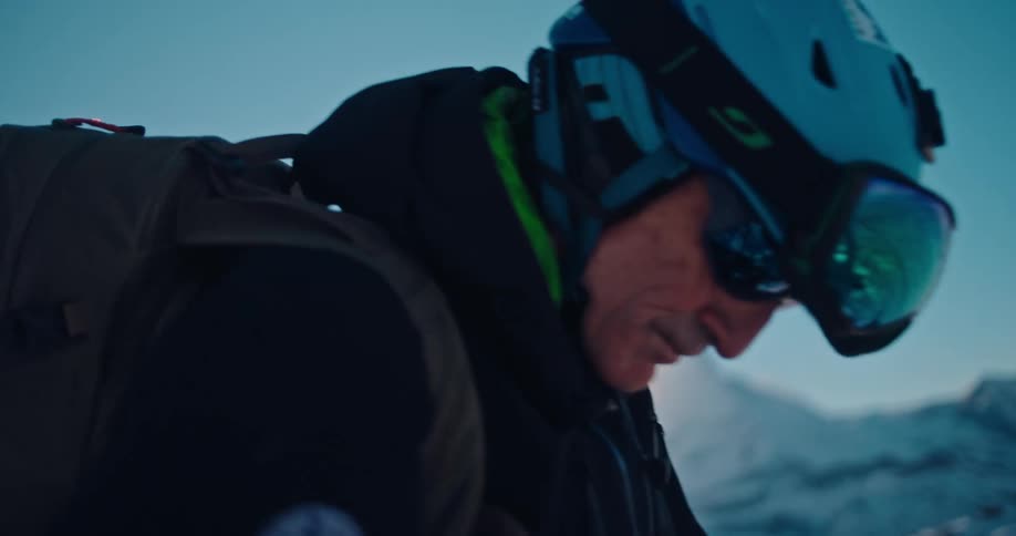 A backcountry skier carefully removes the climbing skin from his ski in the bright snow of the mountains