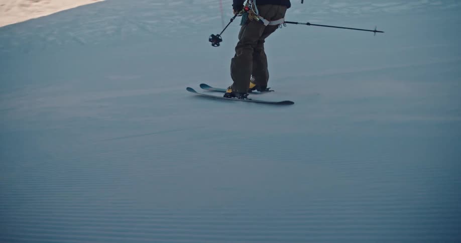 A skier carves down a snowy mountain slope in slow motion with a majestic, sunlit alpine range in the background