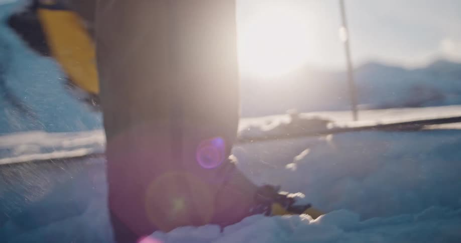 Close-up slow-motion of a skier clicking into their ski bindings in deep powder snow on a sunny mountain