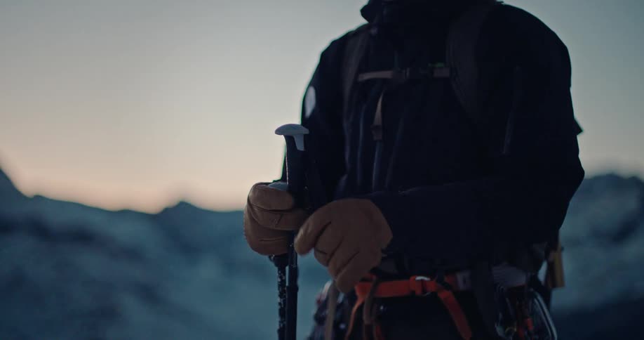 A mountaineer in a snowy landscape carefully adjusts his trekking poles in slow motion at dawn