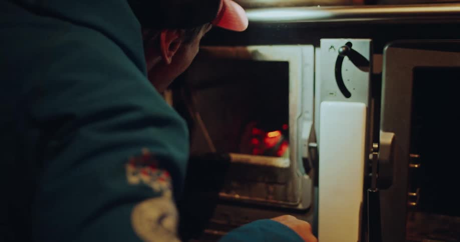 Over-the-shoulder shot of a person adding fuel to start a fire in a rustic wood-burning stove