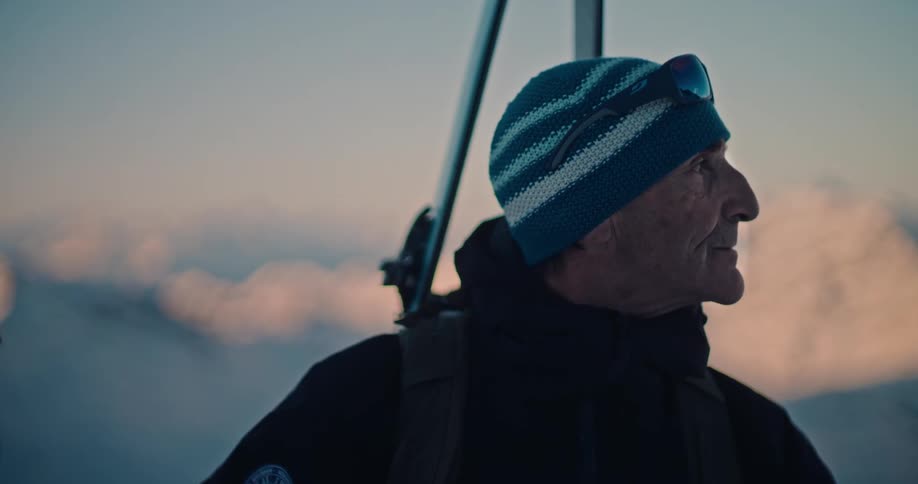 Close-up of an experienced skier looking out over a snowy mountain range with a serene expression at dusk