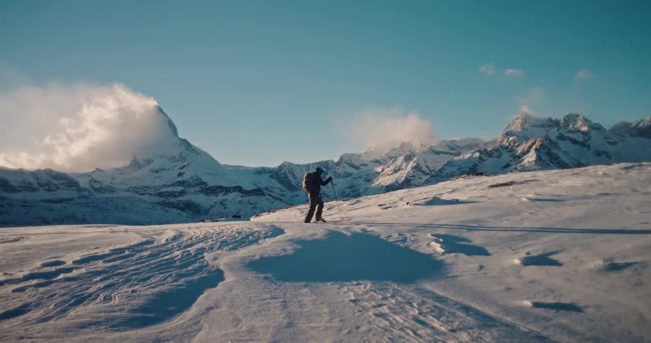 A solo adventurer traverses a pristine snowy expanse in slow motion, with the iconic Matterhorn peak standing majestically in the background