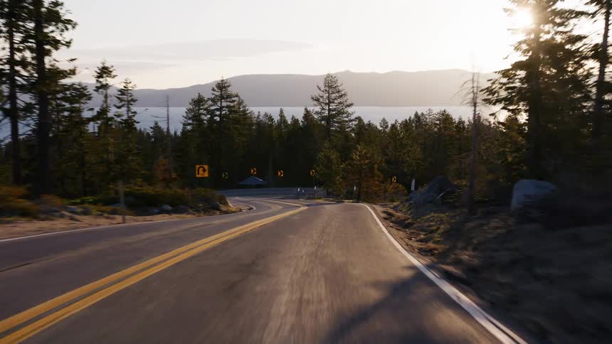 A smooth, scenic drive on a winding mountain road alongside a vast lake during a beautiful golden hour sunset
