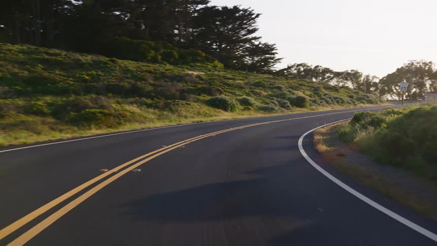 A smooth point-of-view drive along a curving, scenic road through rolling green hills during a brilliant sunrise
