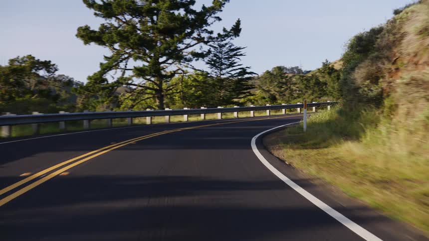 A smooth point-of-view drive along a winding country road surrounded by green hills on a bright sunny day