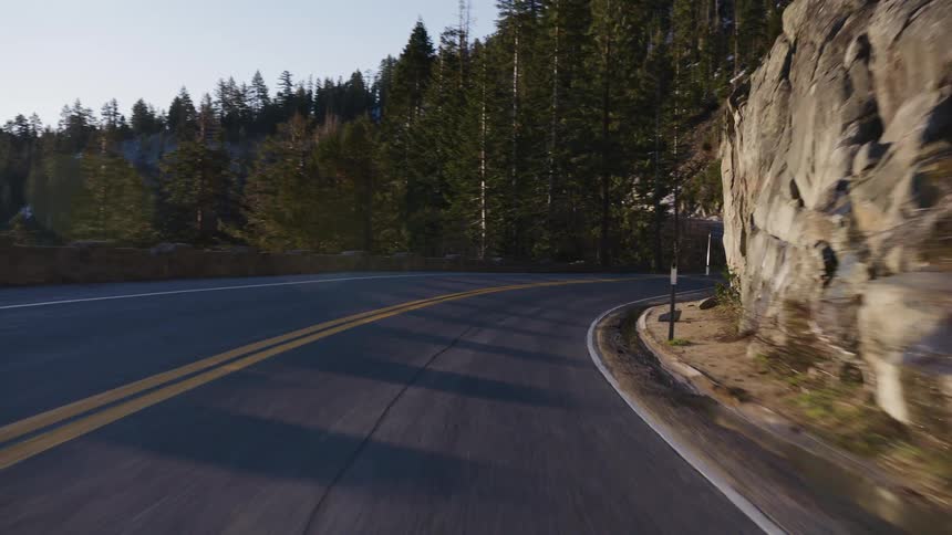 A scenic first-person point-of-view drive on a winding mountain road through a pine forest with rocky cliffs at golden hour