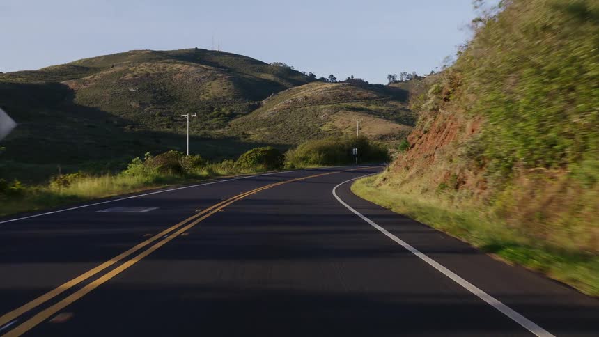 A slow, scenic drive along a winding two-lane road through rolling green hills on a sunny day