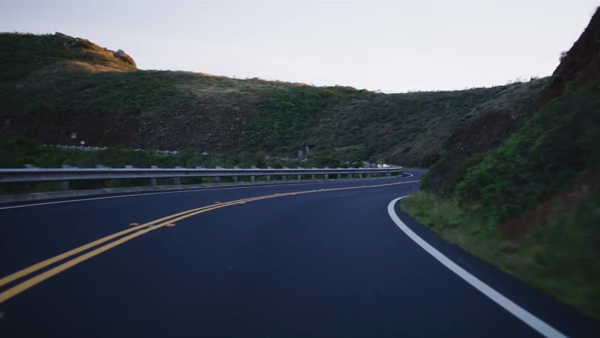 A point-of-view shot smoothly navigates a winding country road through rolling green hills at dusk
