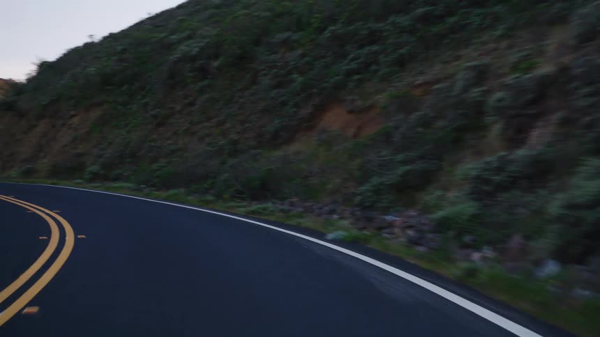 A smooth point-of-view drive on a winding mountain road at dusk