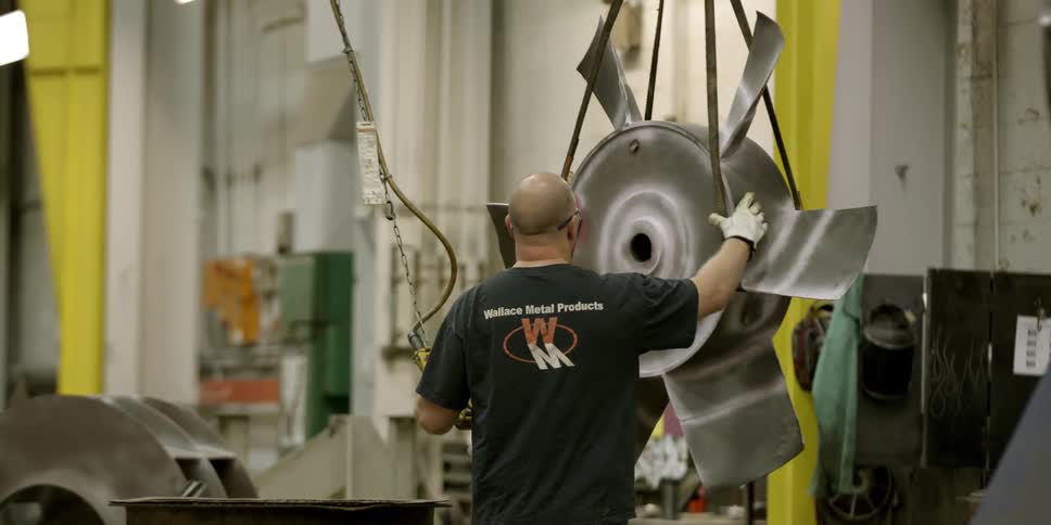A man guides a large rotor he is moving with an electronic cable hoist