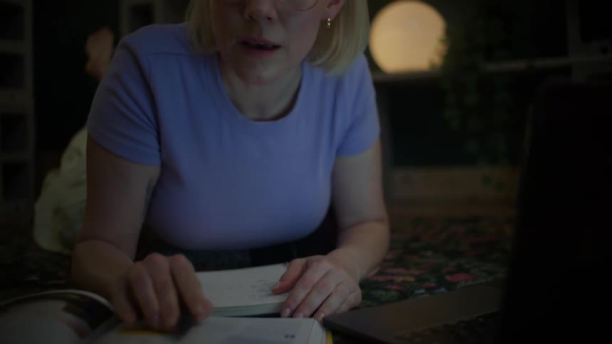 A focused young woman with glasses studies late at night, lying on the floor with her laptop and textbooks