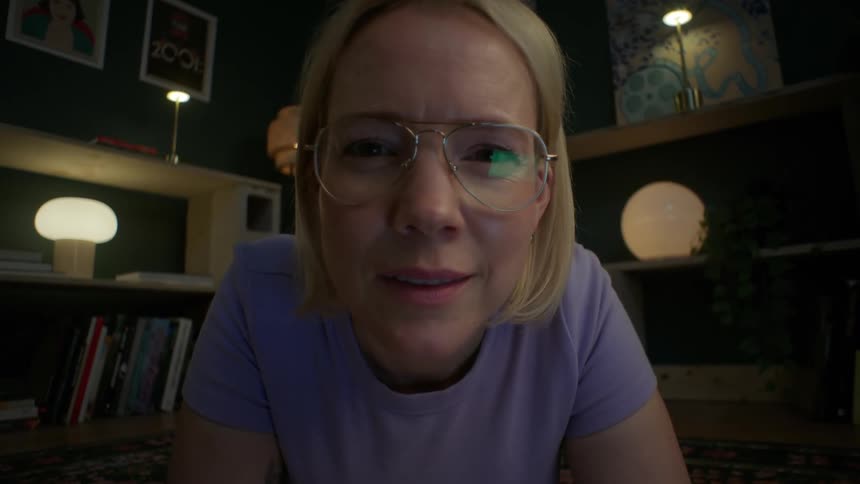 A woman's face is illuminated by a screen as she watches something that makes her smile in her cozy living room at night