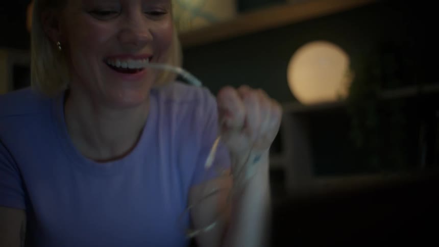 Happy young woman laughing while working on her laptop at night, putting on her glasses as she smiles