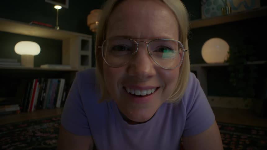 Point-of-view shot of a woman with glasses on a video call at night, her expression changing from serious to a joyful smile